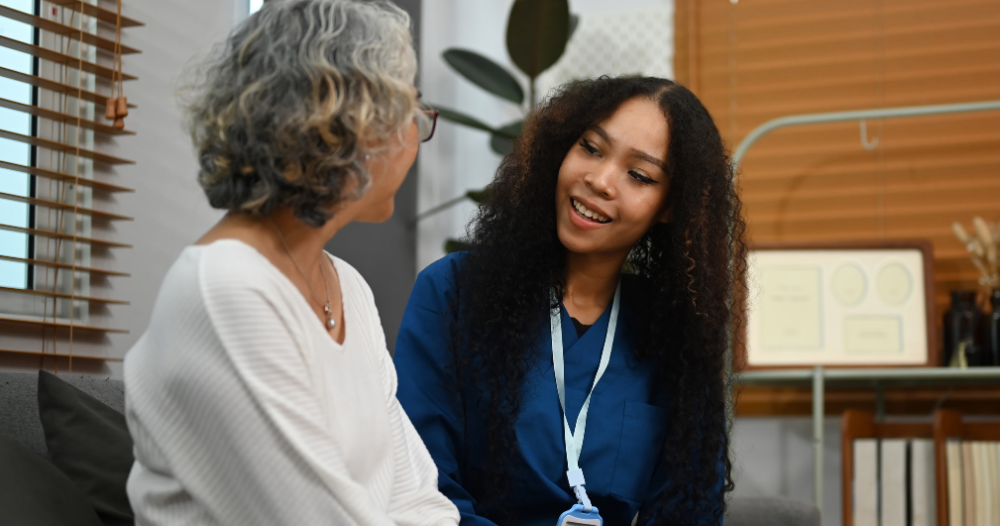 A caregiver patiently and kindly sits down and talks with a senior client, setting a good example for caregivers when it comes to communication.