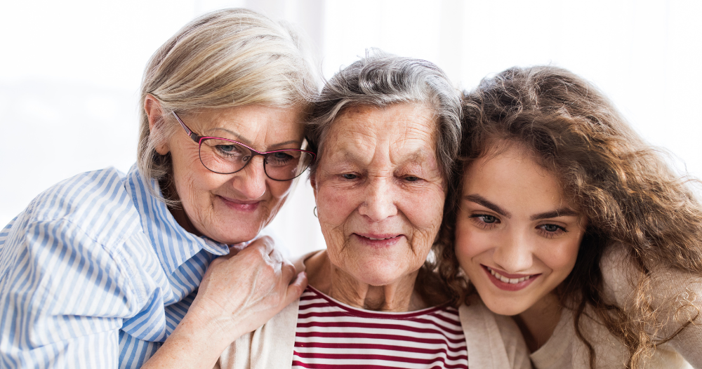 Three generations embrace and look at a computer, representing the sandwich generation.