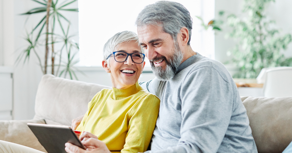 A senior couple smiles while looking at a laptop, showing how online resources can help family caregivers.