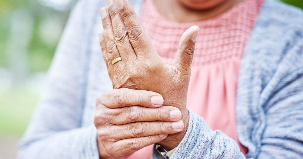 A senior woman holds her hand in pain, representing arthritis and what Arthritis Awareness Month can help with.