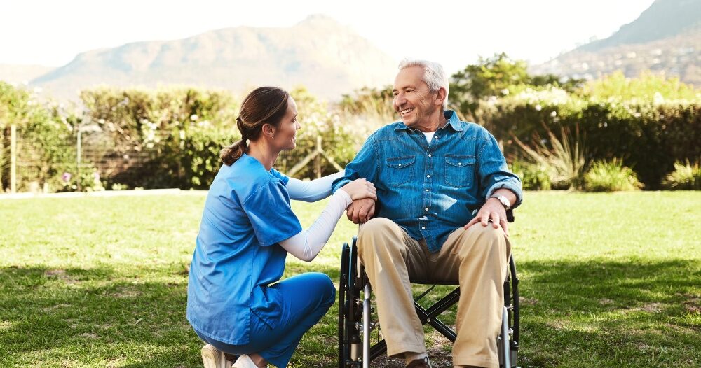 Caregivers like this one talking to a smiling senior patiently and compassionately help clients and help them with aging in place while dealing with different conditions.