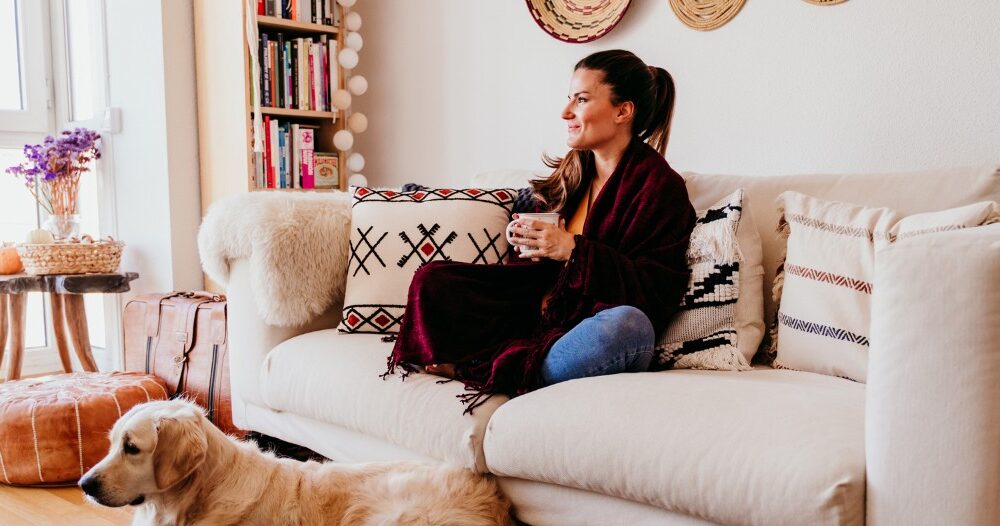 A woman relaxes with her dog while sipping on tea, representing how self-care can combat caregiver stress.