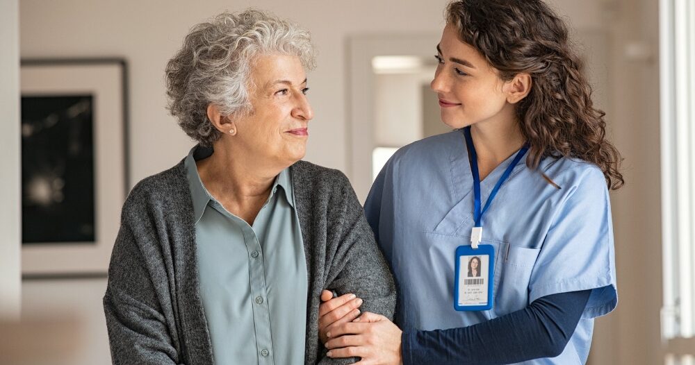 A caregiver and client smile at each other as the caregiver helps the client, representing emotional intelligence in caregiving.