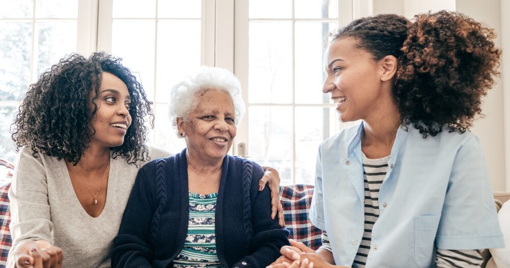 A caregiver talks with a client and her daughter, representing the type of communication that is vital when taking on a person-centered care approach.