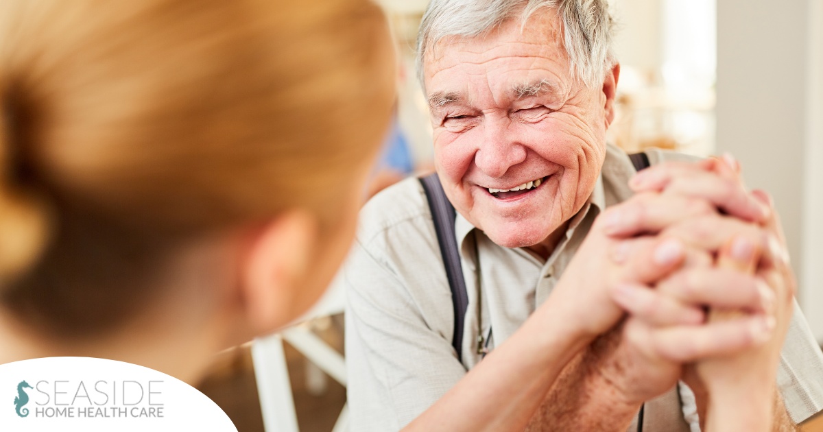 A caregiver holds hands with a happy older client, representing the results of creating a comfortable environment in the home.