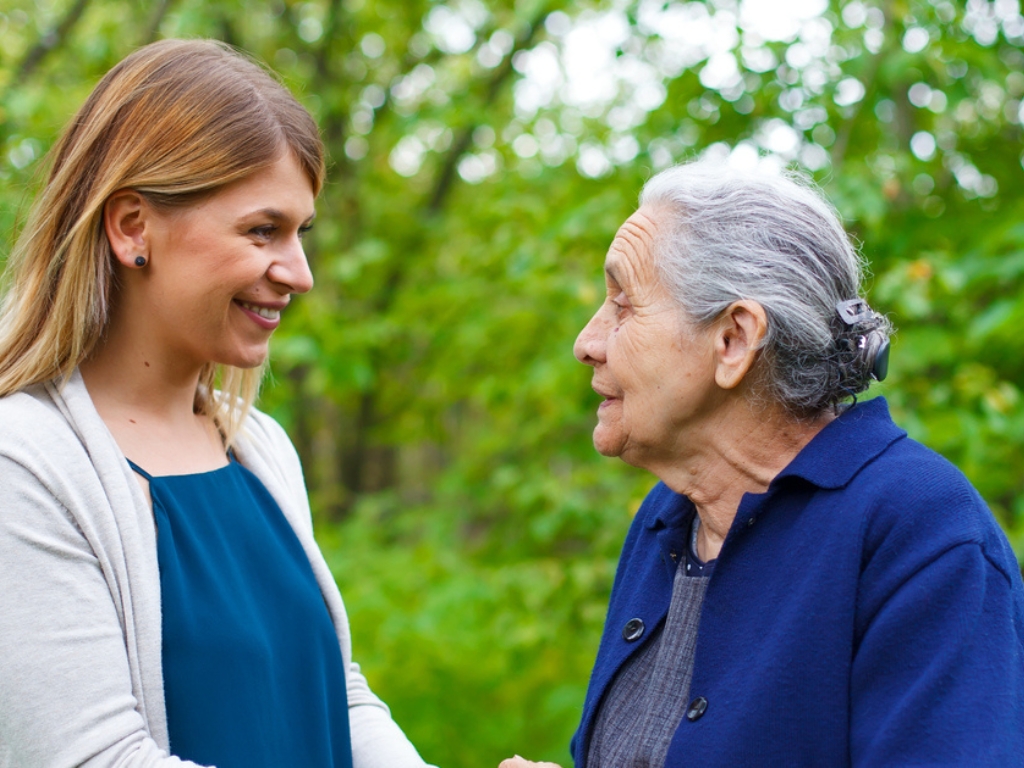 Lehigh Acres A cheerful caregiver assists and elderly woman on a walk outside with green trees in the background.
