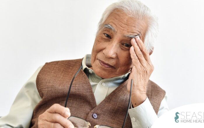 An older adult holds his head and his glasses representing vision problems like macular degeneration.