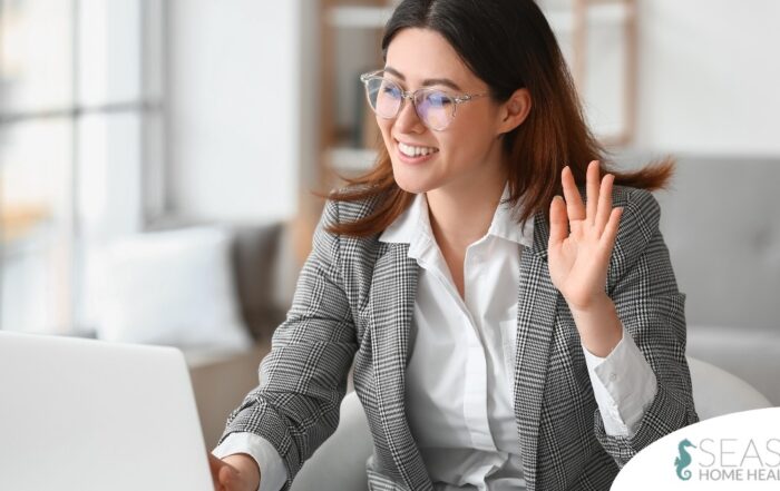 A well-dressed woman smiles and says hi on a videoconference, representing a candidate who is well-prepared for a caregiver interview.