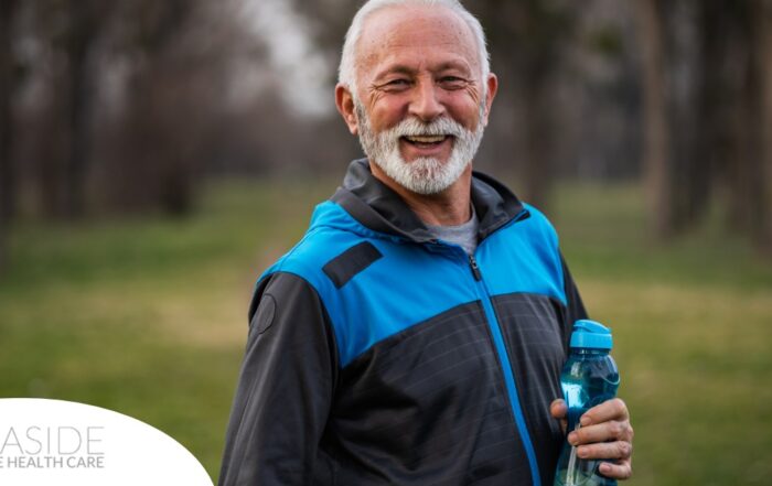 An older man smiles with a water bottle while exercising, representing the benefits of encouraging exercise when caring for seniors at home.