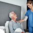 A caregiver smiles at an older client in bed, representing the compassion involved in being a live-in caregiver.