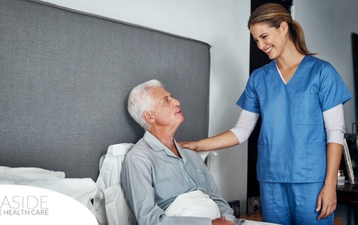 A caregiver smiles at an older client in bed, representing the compassion involved in being a live-in caregiver.